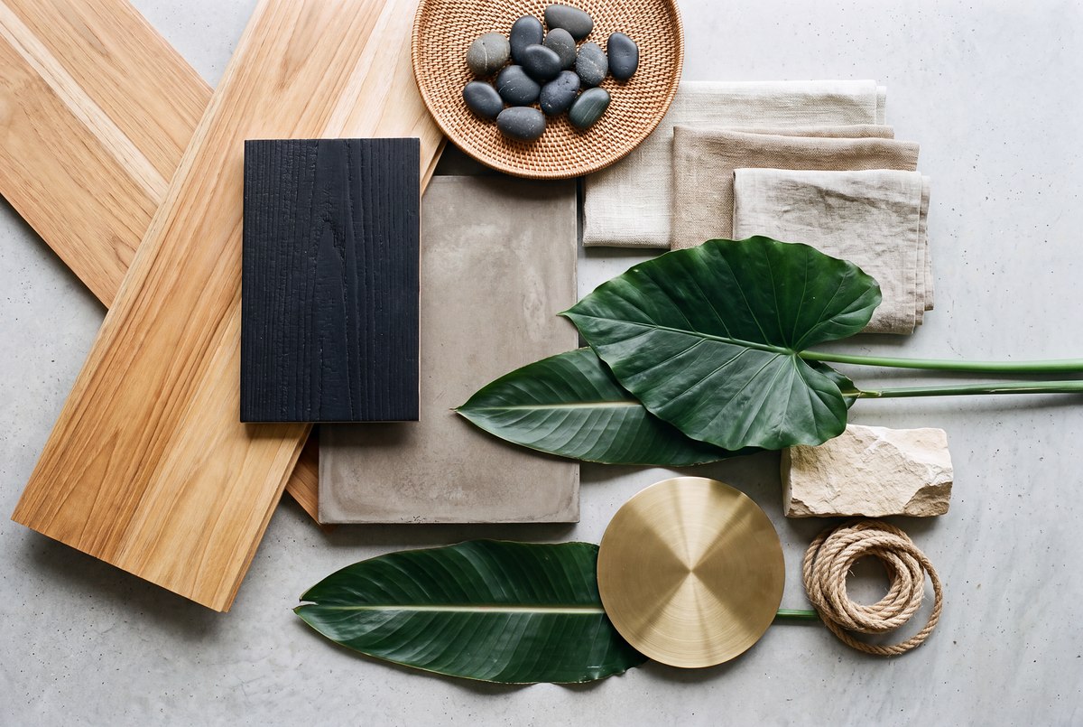 The 4 Elements Sanctuary material palette laid out flat — pale Loréal hardwood with heavy open grain, charred black timber, board-formed concrete, woven flax and linen textiles, local river stone and limestone, native tropical foliage, brushed brass and natural rope